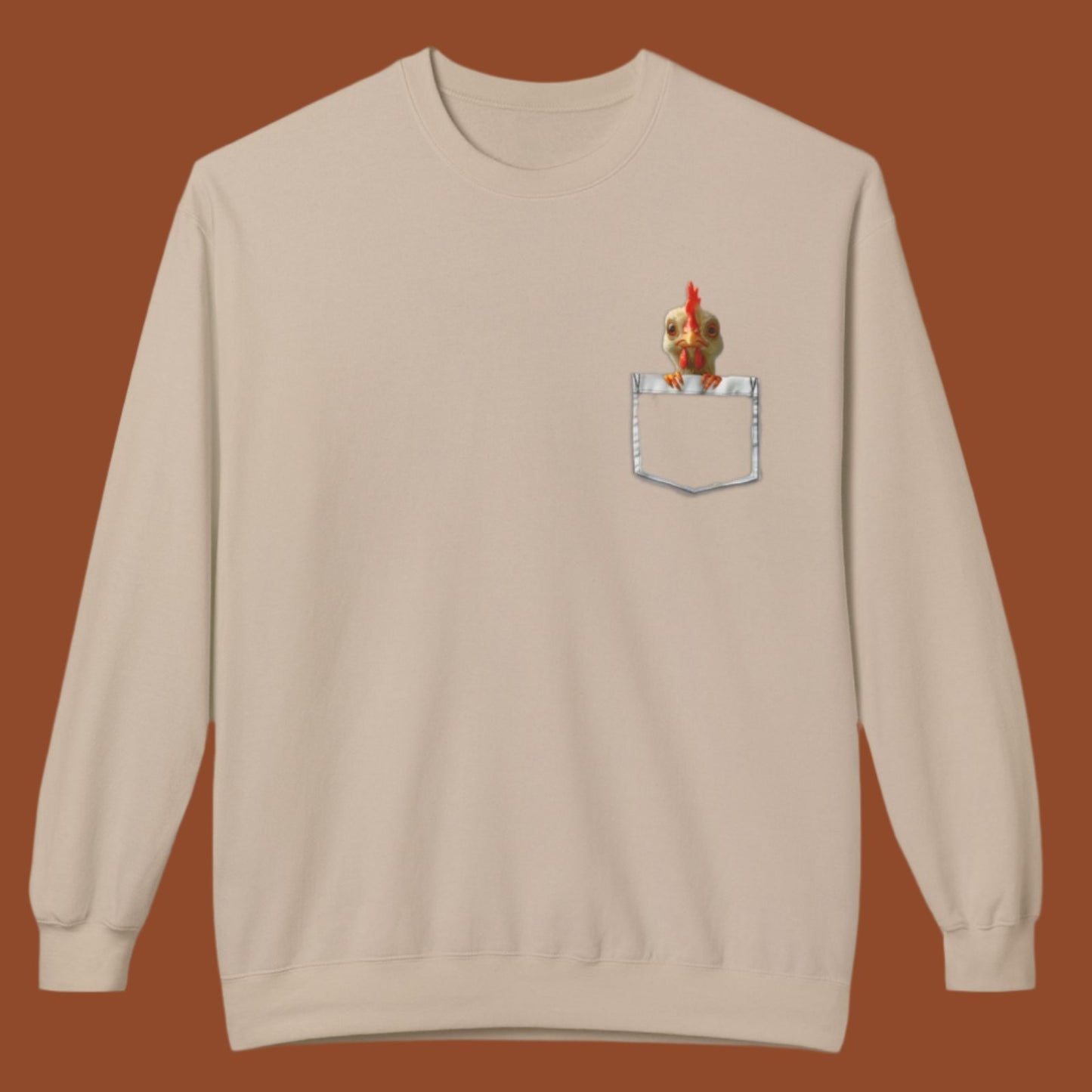 a sand colored sweatshirt has a printed front pocket with an orange young chicken sticking its head and front claws out of the pocket. Pocket Pals! Only from The Curated Goose